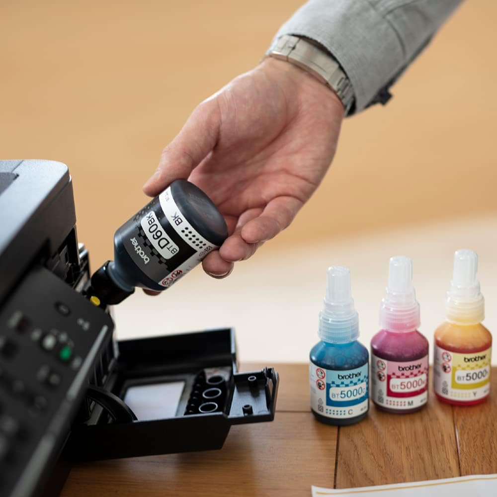 Hand refilling Brother ink tank printer with colored ink bottles beside the ink compartment