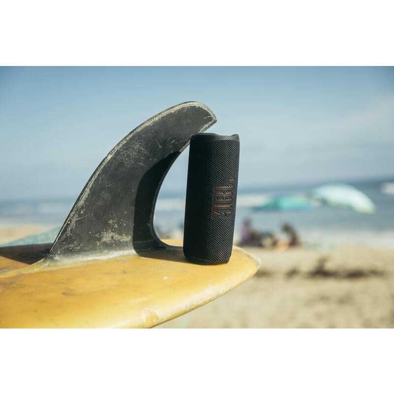 JBL Flip 6 portable speaker standing on a surfboard near the shoreline