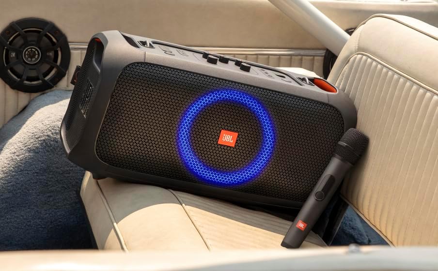 Black JBL microphone lying near a portable speaker, with wire-mesh grille and side switch