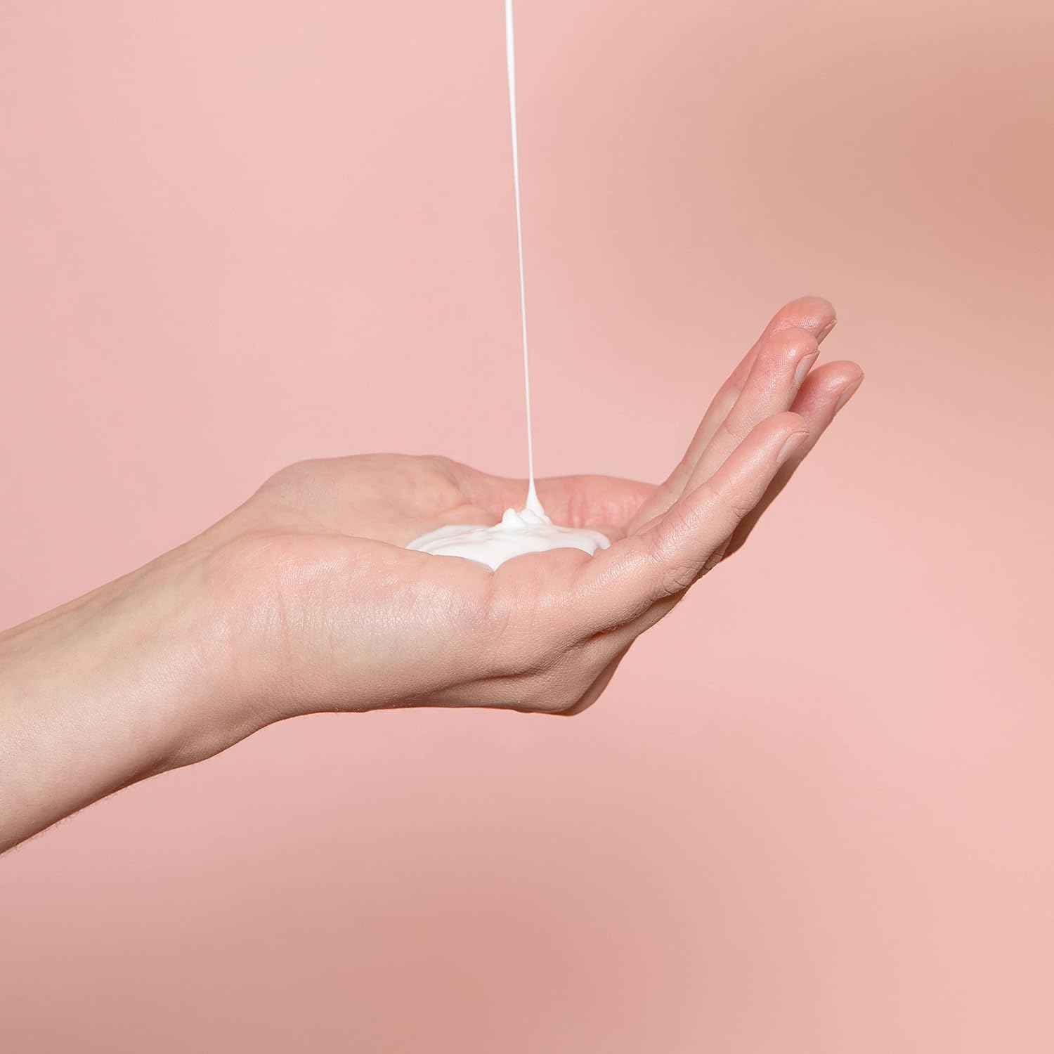 Hands applying white body moisturizer from bottle pump