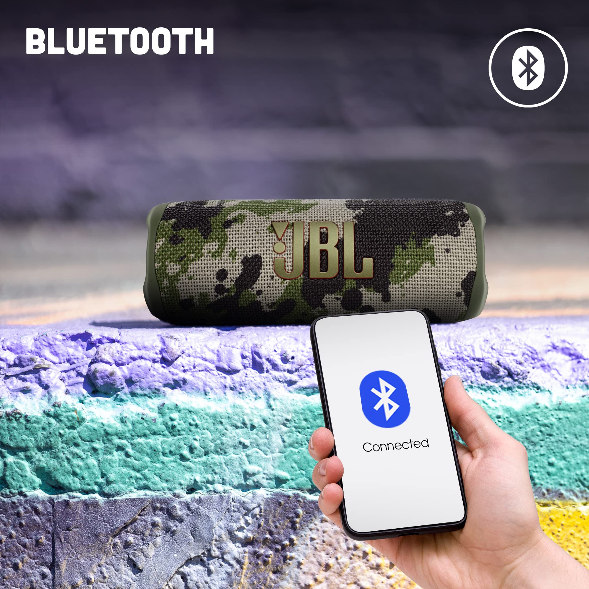 Camouflage JBL Flip 6 speaker with a hand holding a connected Bluetooth phone