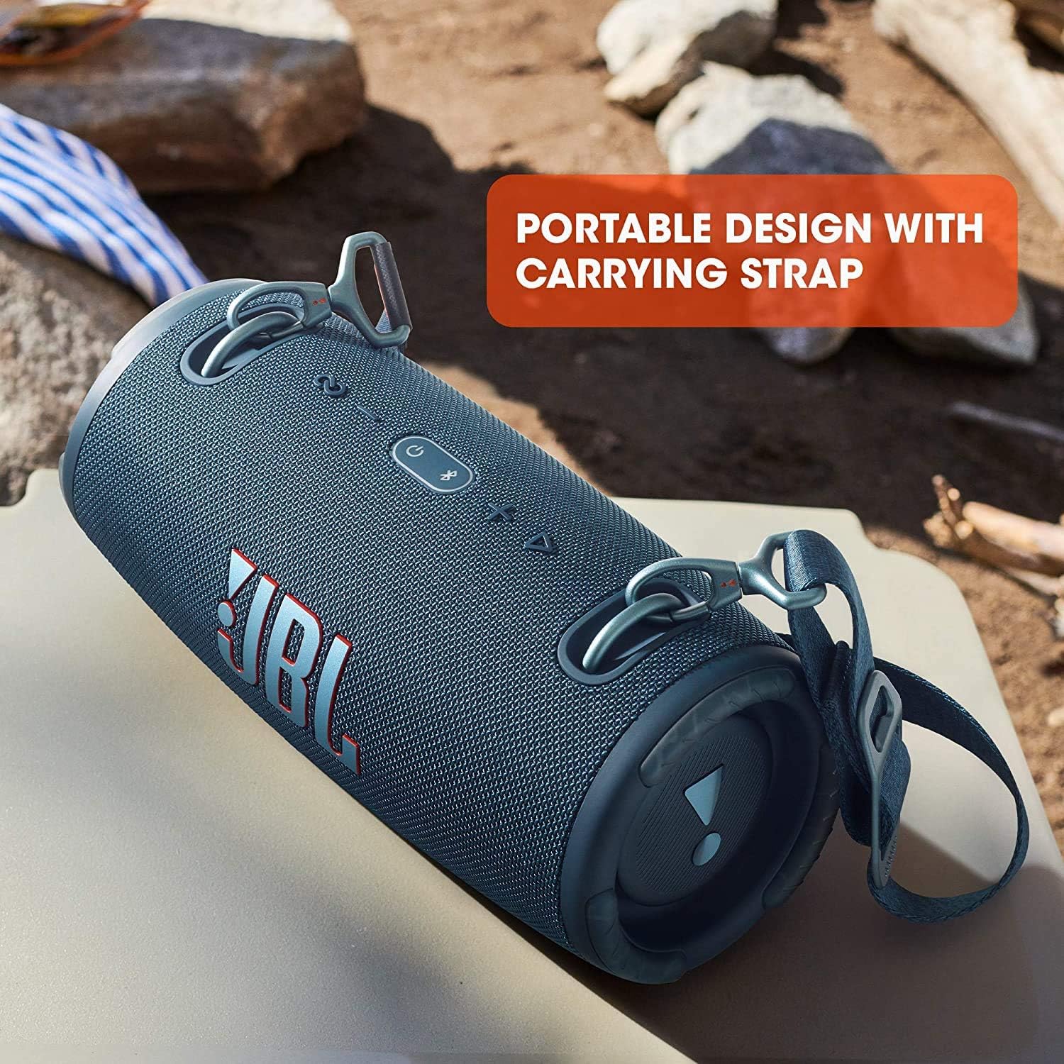 Portable waterproof speaker with dark fabric body and carrying strap, tilted on surface