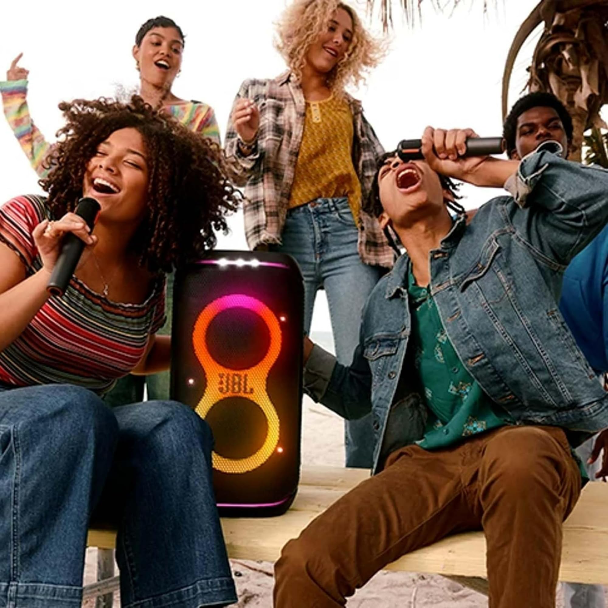 Group singing with handheld mics while a JBL PartyBox speaker shows purple LED lights