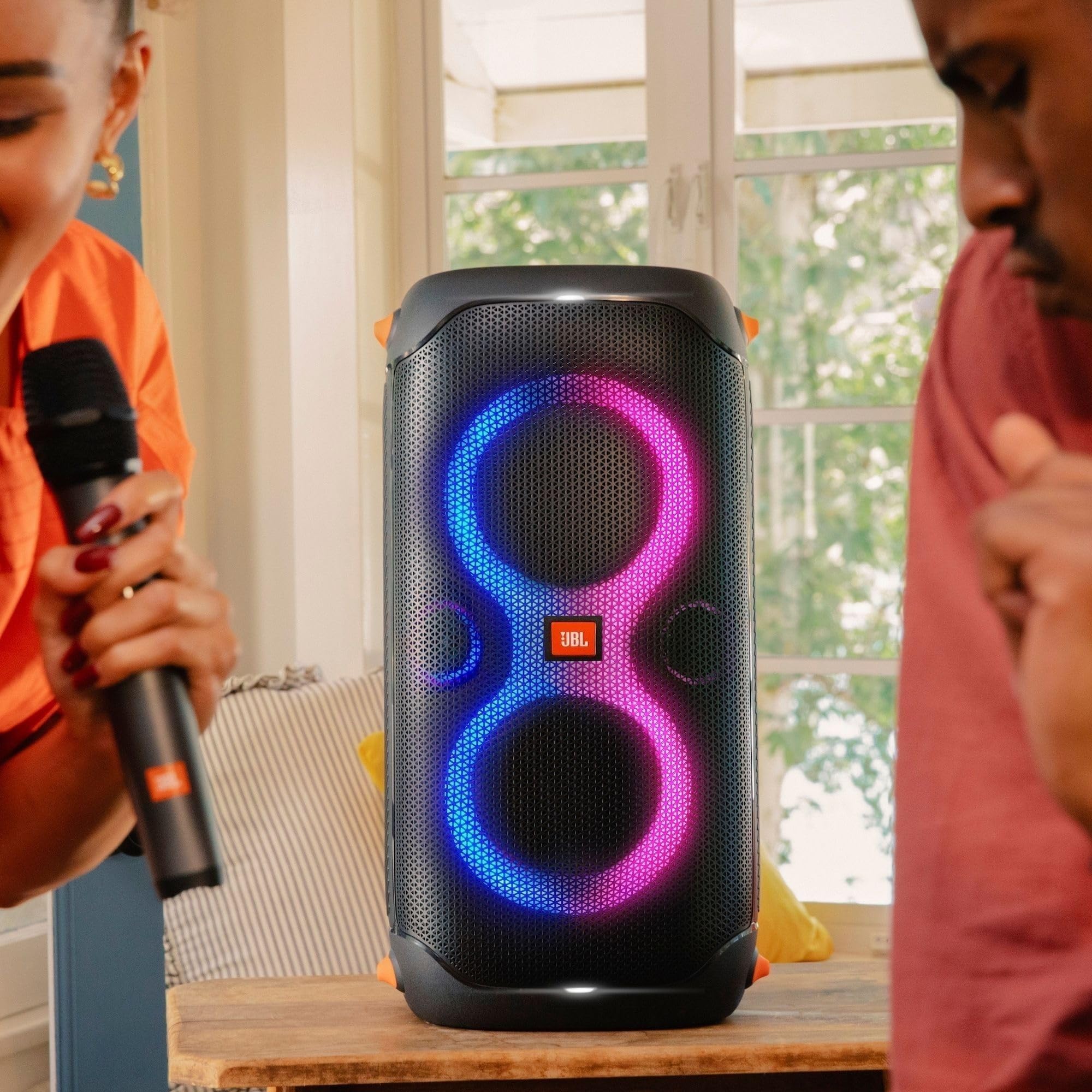 Black portable party speaker with blue LED rings on a table with wireless microphones.
