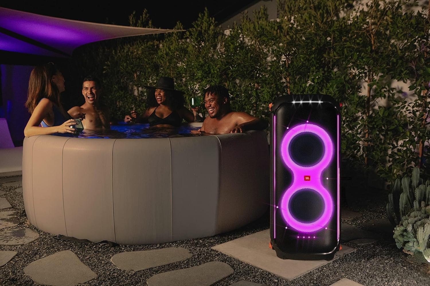 Outdoor backyard party with a JBL PartyBox speaker showing purple glowing LED rings