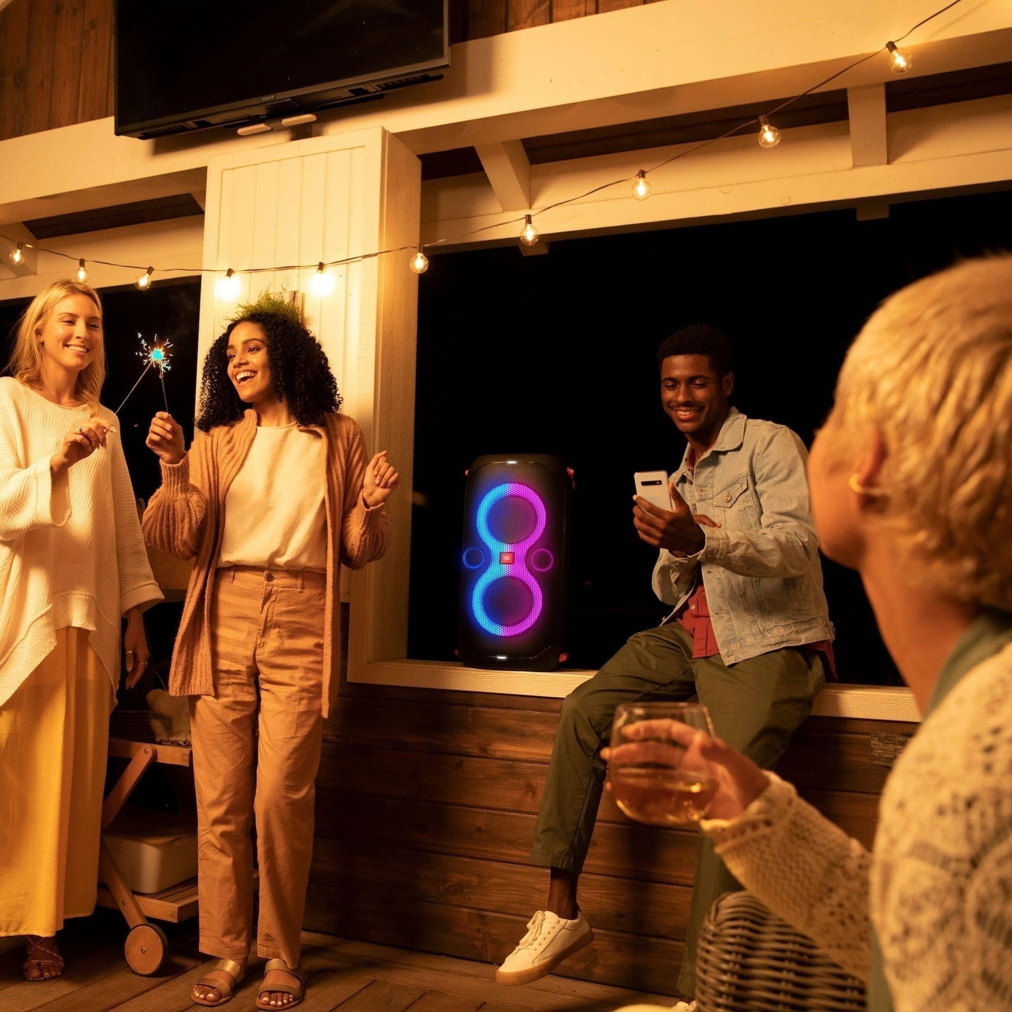 Portable party speaker with glowing LED rings with people holding wireless handheld microphones indoors.