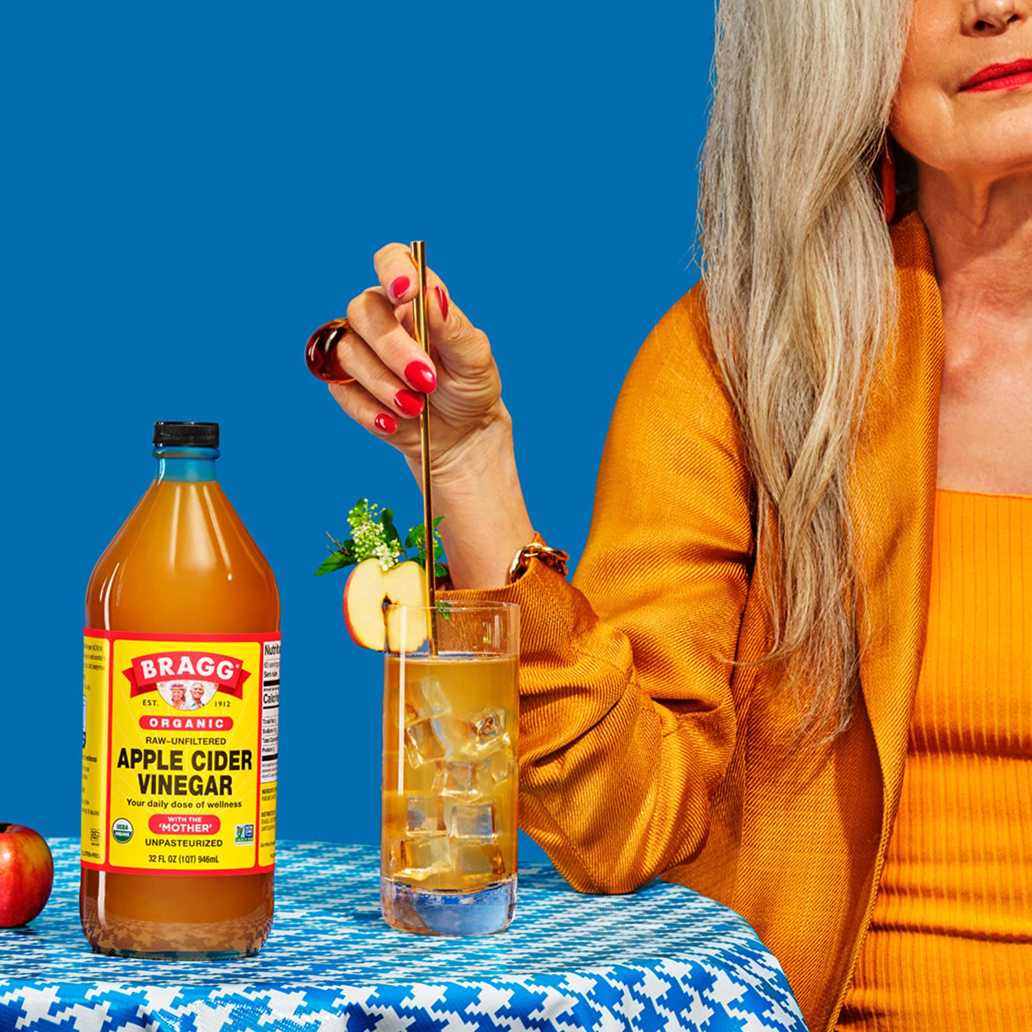 Bragg apple cider vinegar bottle near a glass of clear liquid being poured at a table.