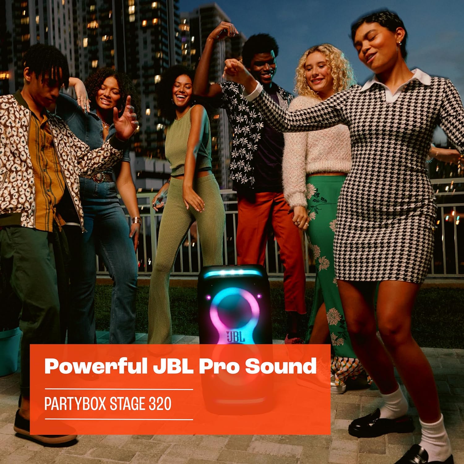 Portable JBL PartyBox speaker with glowing multicolor LED lights at an outdoor gathering