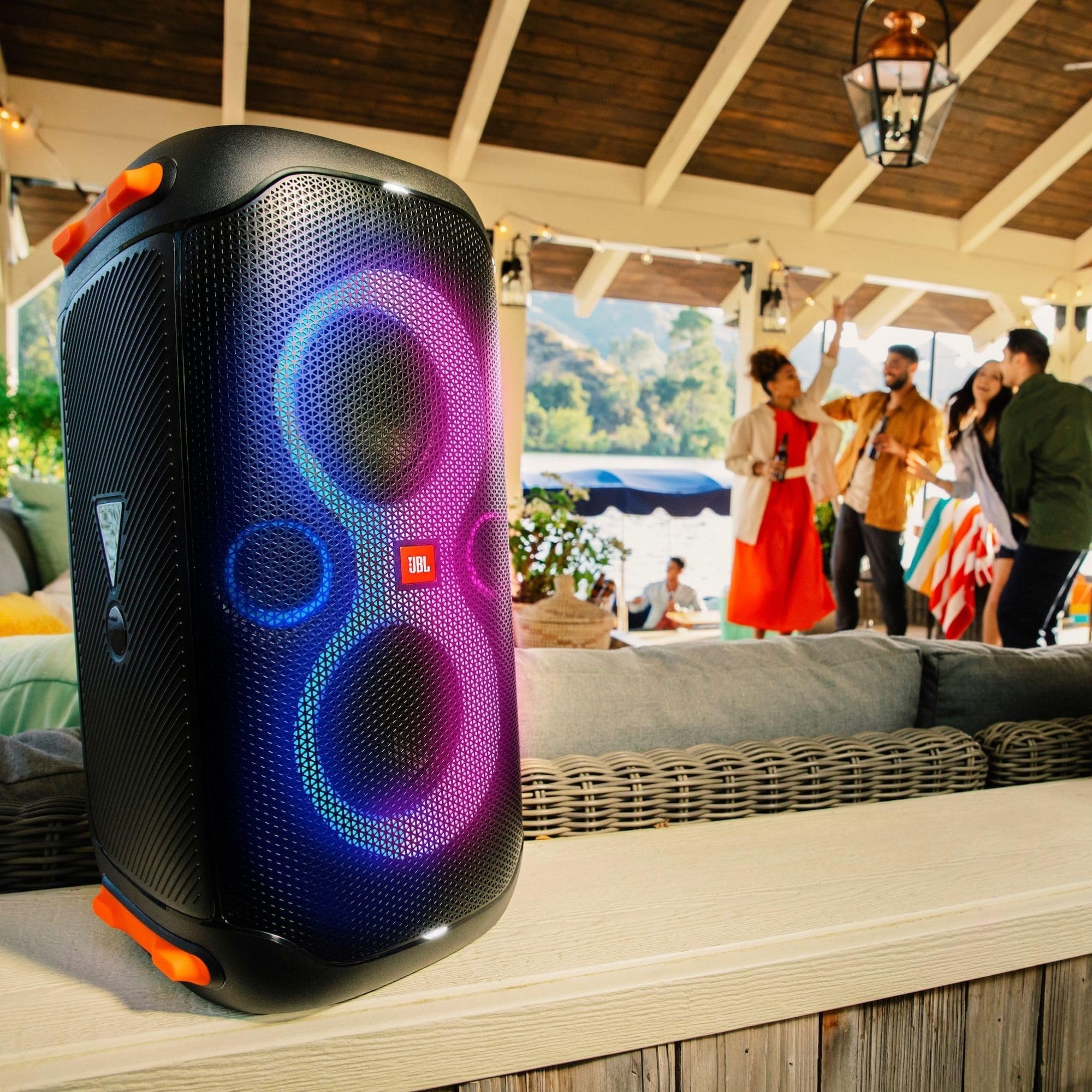 Black portable party speaker with purple-blue LED rings on outdoor seating with wireless mic.