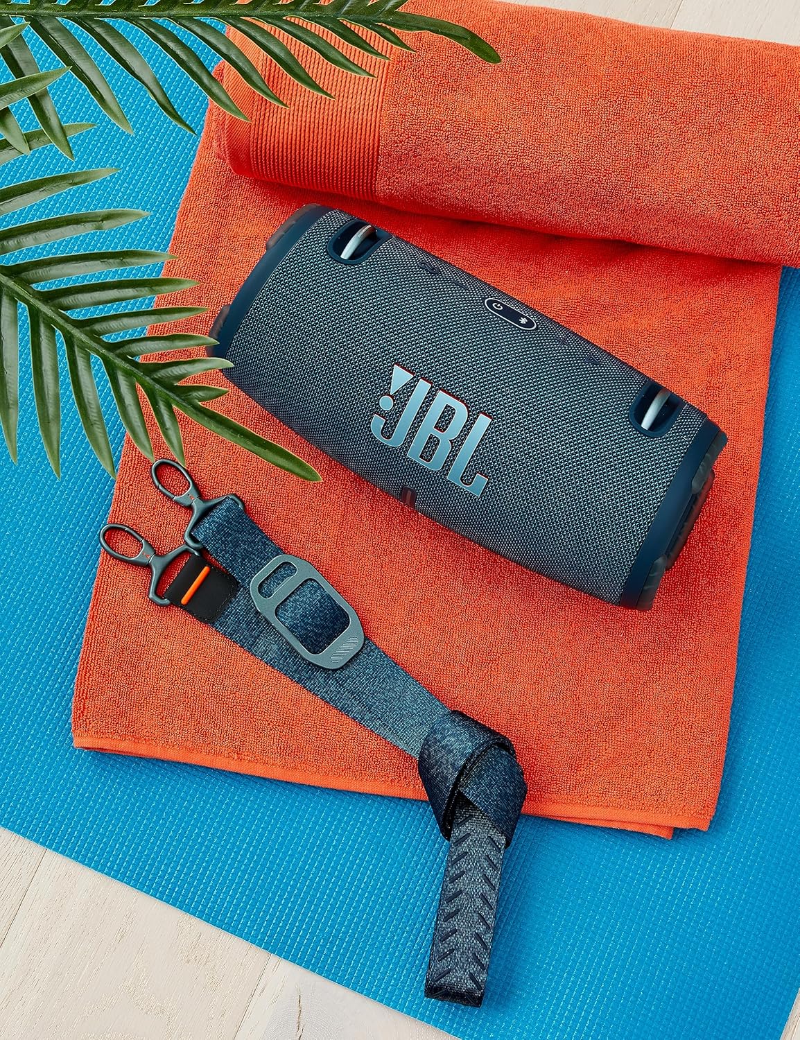 Blue portable waterproof speaker on an orange and blue towel with strap