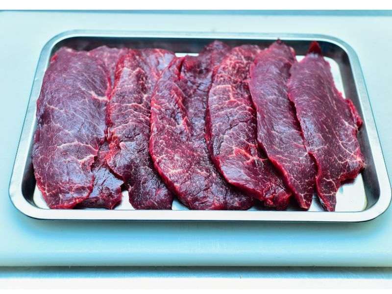 Sliced beef steak with visible marbling, arranged in a metal tray