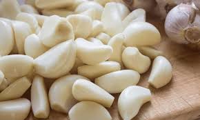 Peeled garlic cloves, 1 kg pack; whole and broken cloves on a wooden surface