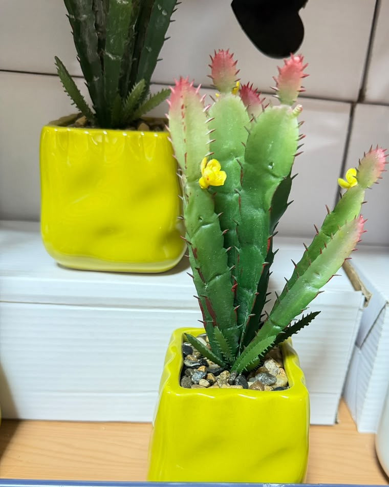 Artificial cactus plant with pink flower buds in a small bright yellow square planter