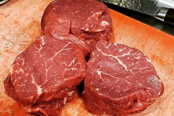 Raw beef fillet steak pieces, trimmed, on a cutting board